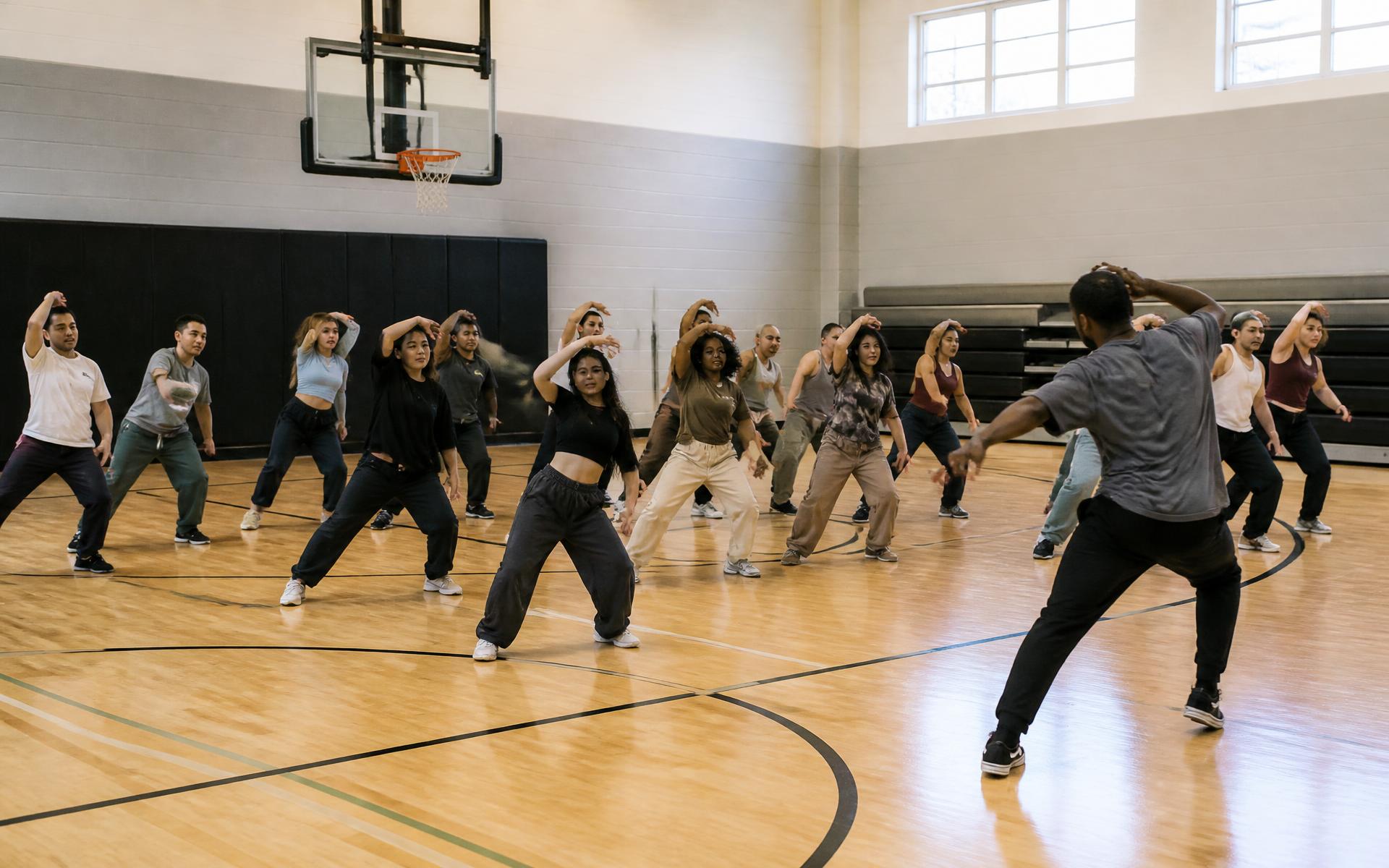 A dance class underway on a school gym basketball court with an instructor leading